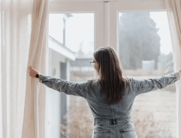 Gordijnen.nl (1) Woman from backside in denim outfit opening beige curtains