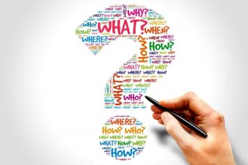 Hand holding a pen pointing to a question mark that is filled with question words